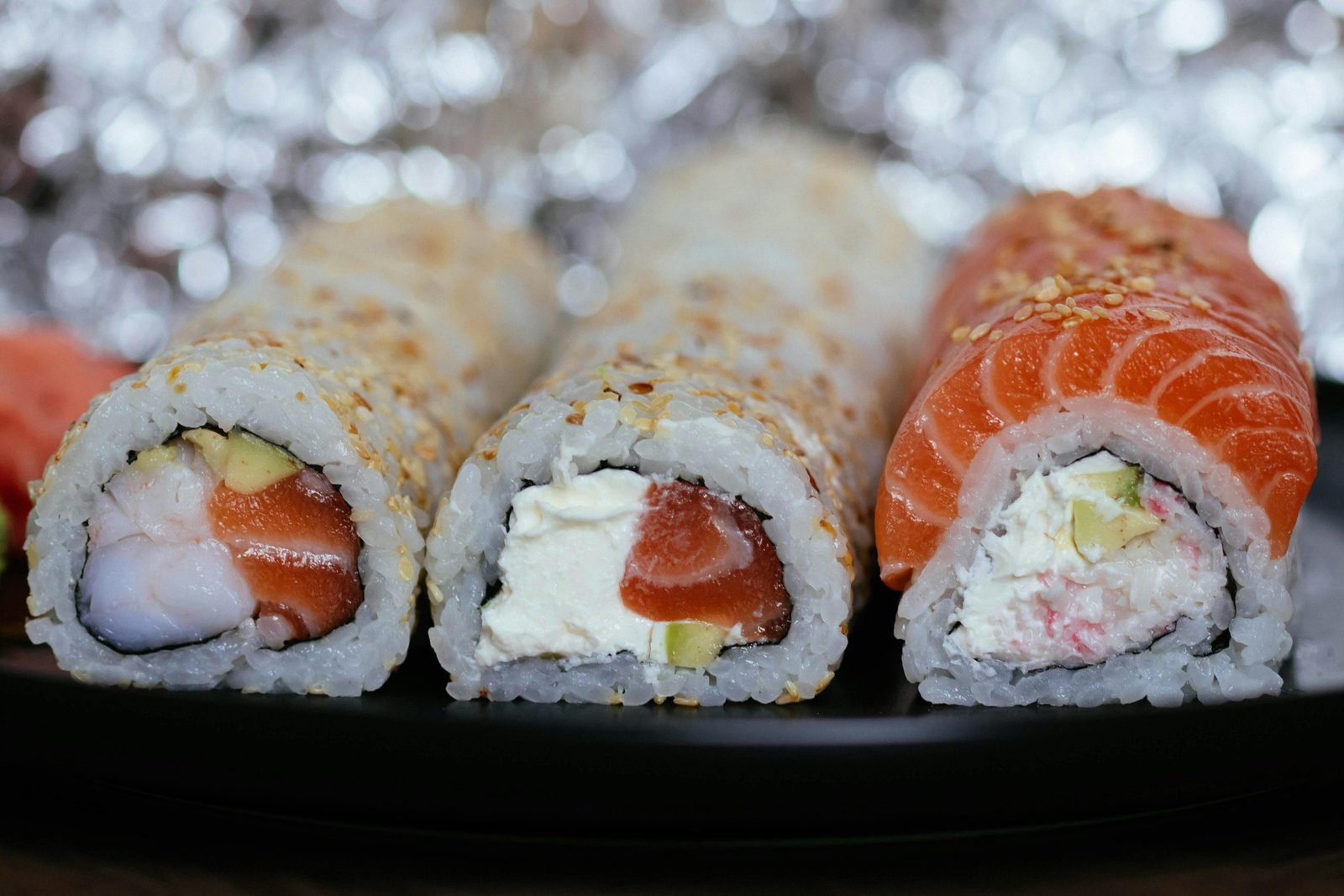 Tempting close-up of assorted sushi rolls with salmon and cream cheese on a black plate.